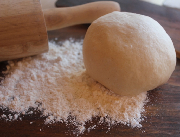 A ball of pizza dough and flour on a wood table